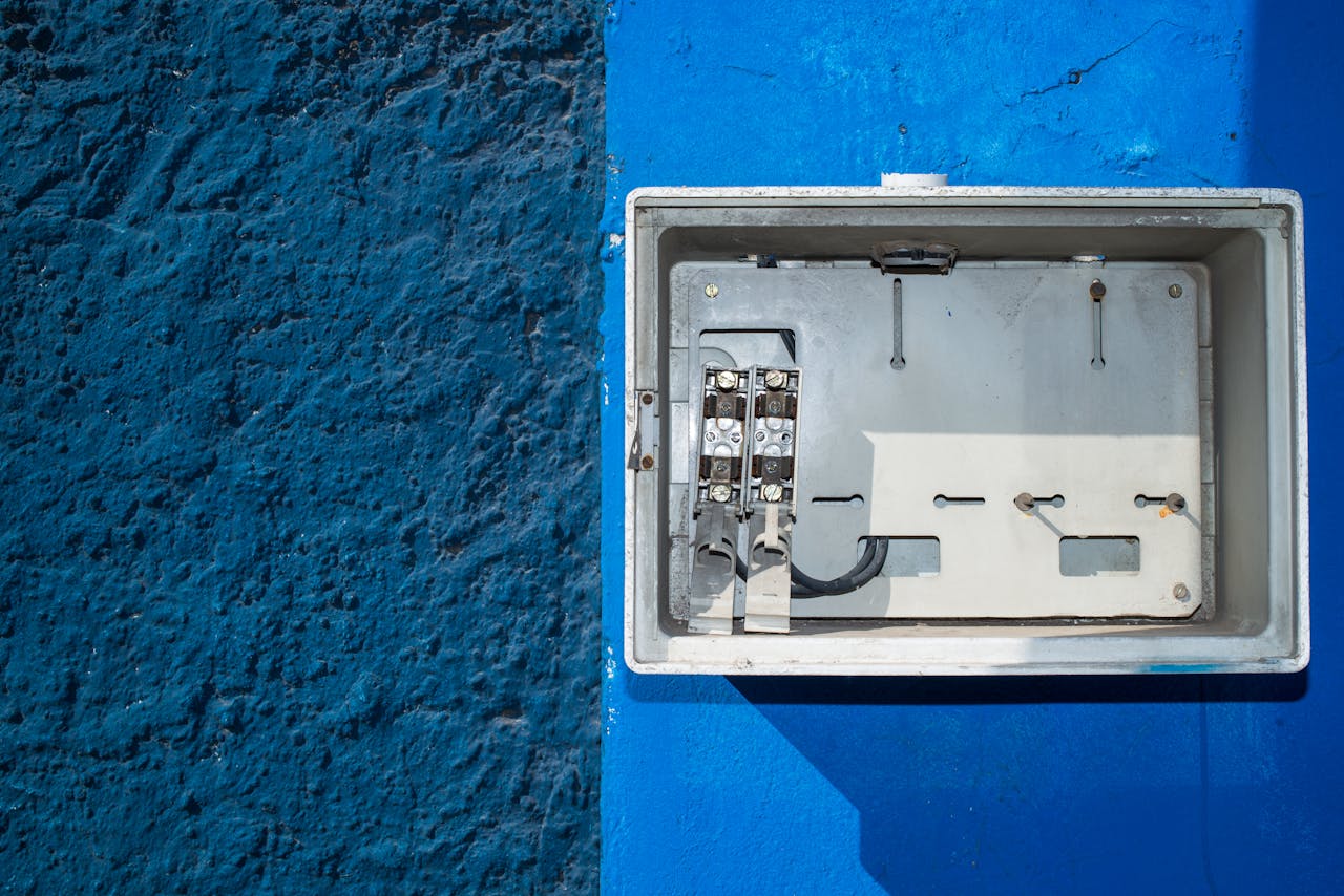 A weathered electrical panel on a vivid blue wall, blending industrial and artistic elements.